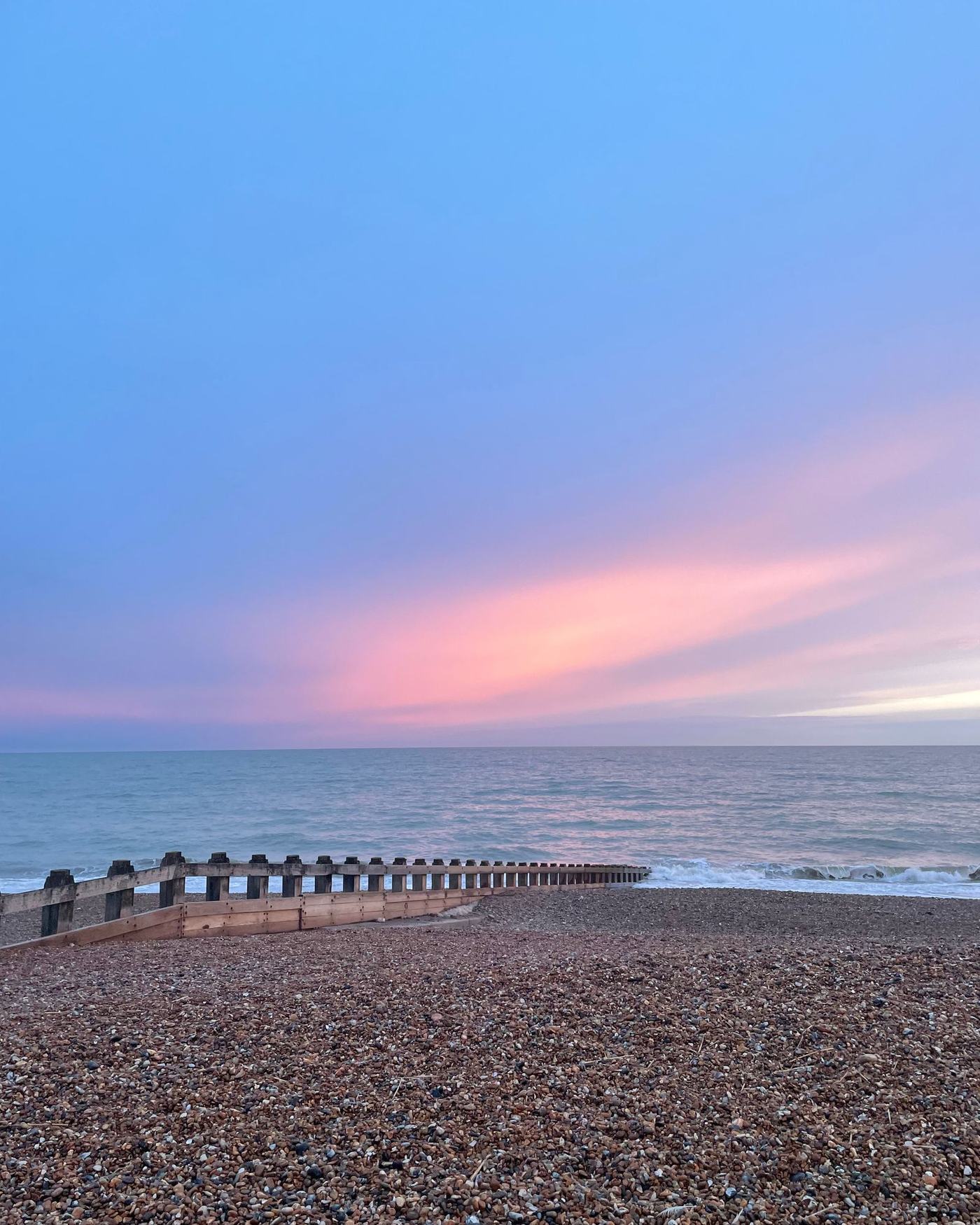 A pastel evening sky over the pebble beach and wooden groyne below the sea wall