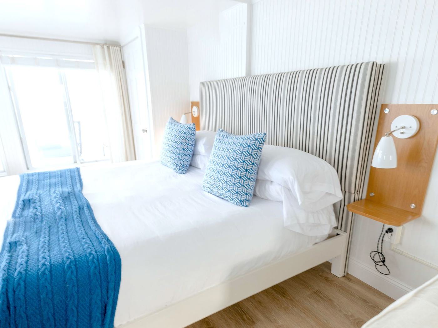 A bright coastal suite with white panelling, a striped headboard and blue cushions