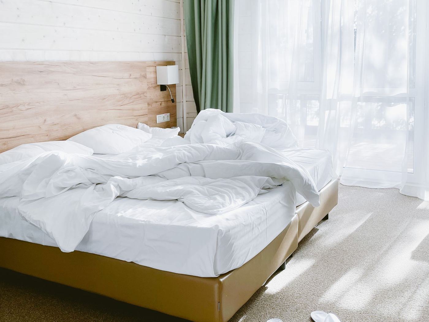 A light-filled bedroom with white bedding and soft morning sun through sheer curtains